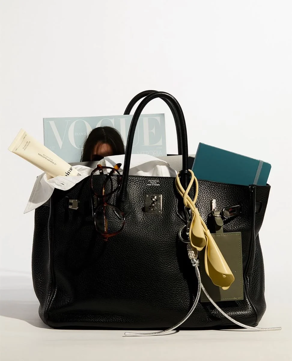 A black Hermès Birkin packed too full to close, with a French Vogue, a white shirt and a notebook sticking out of the top