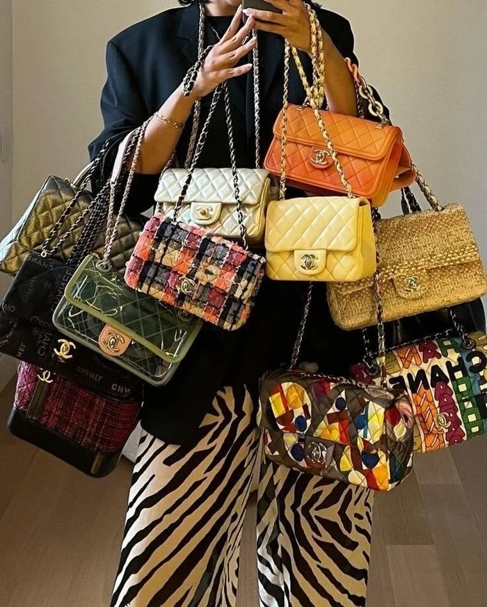 Someone holding a dozen vintage Chanel flap bags in every colour, over zebra-print trousers
